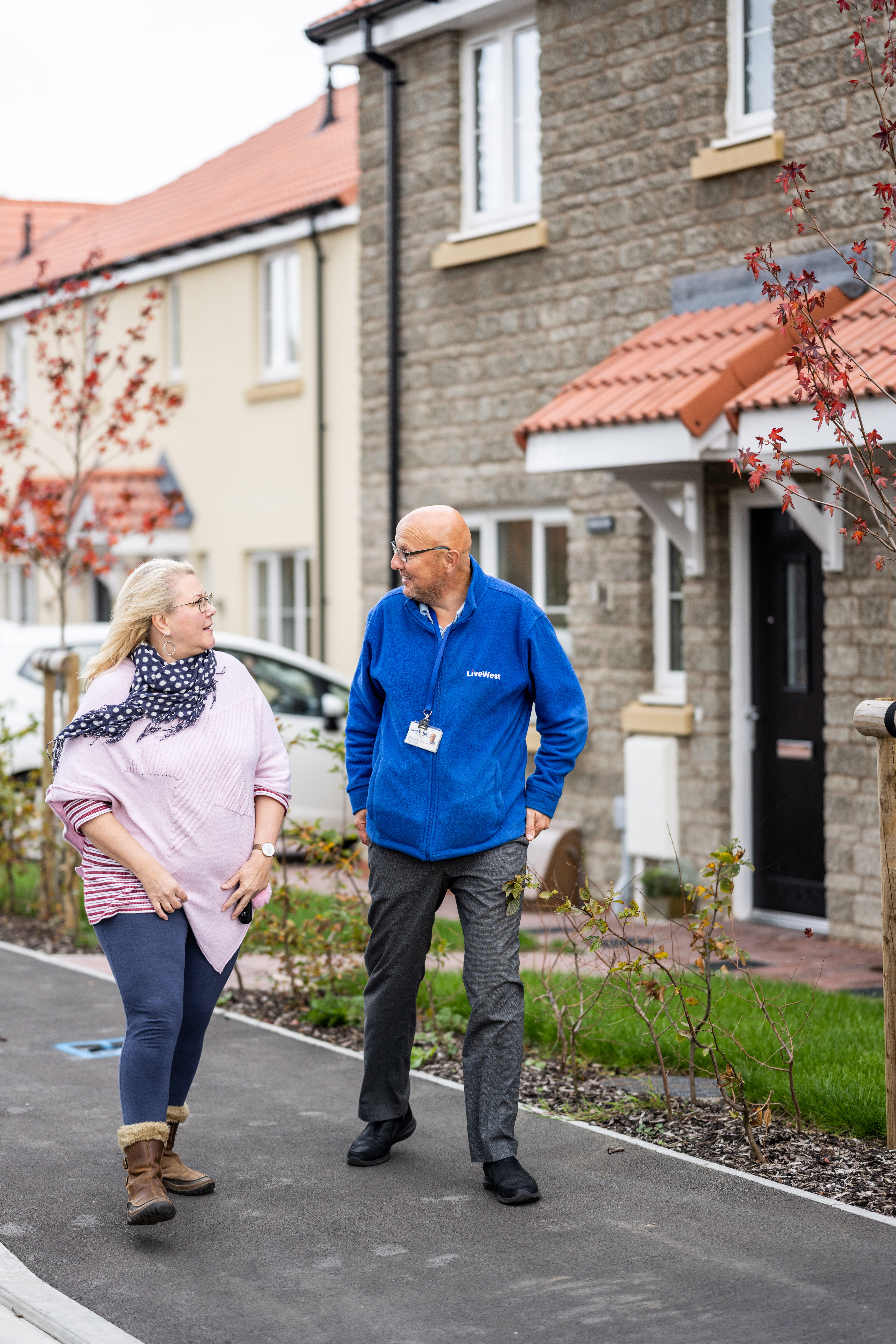 A man and a woman are walking and talking together on a pavement in a residential area.