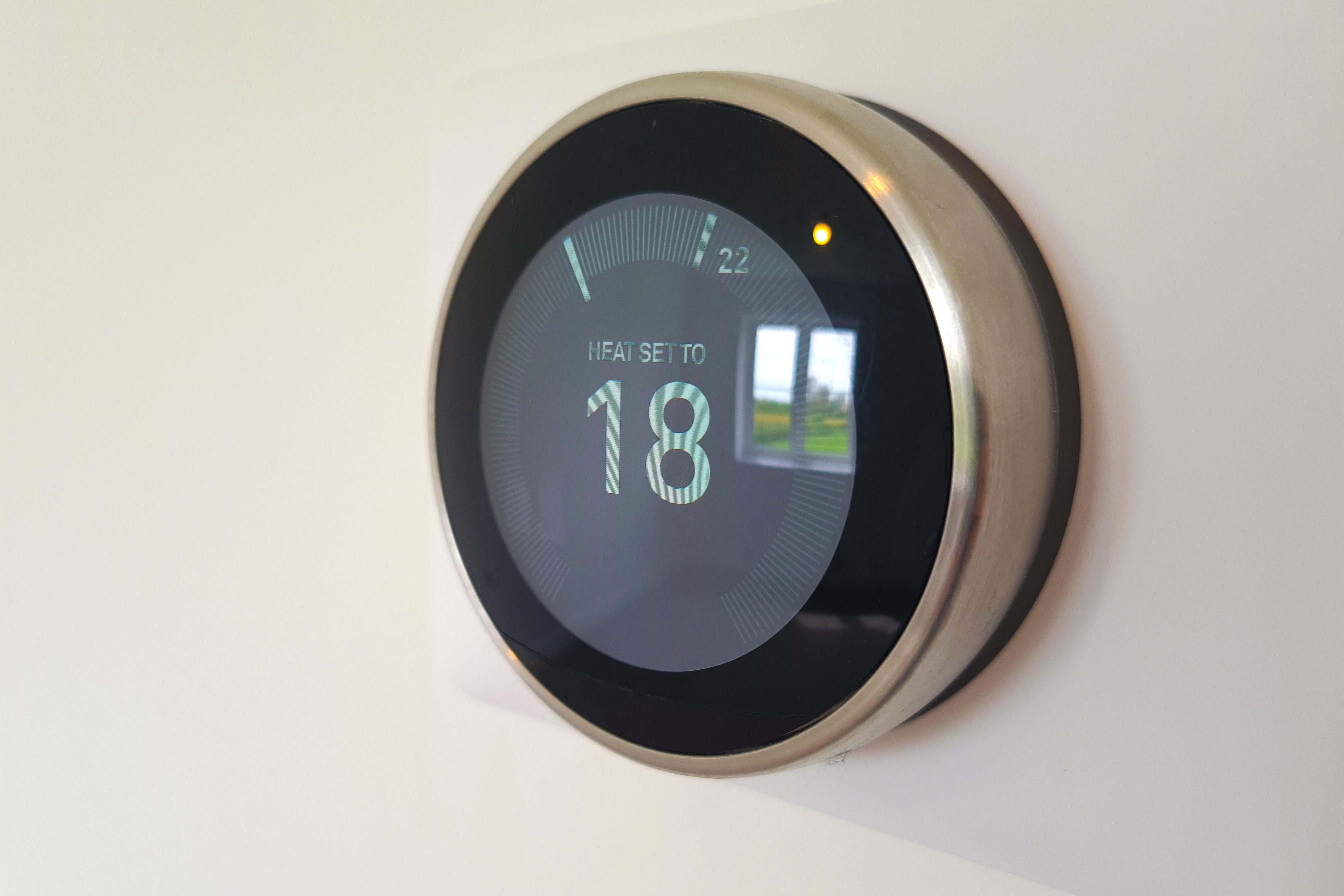The main subject is a digital thermostat set to 18 degrees, mounted on a plain wall in a home.
