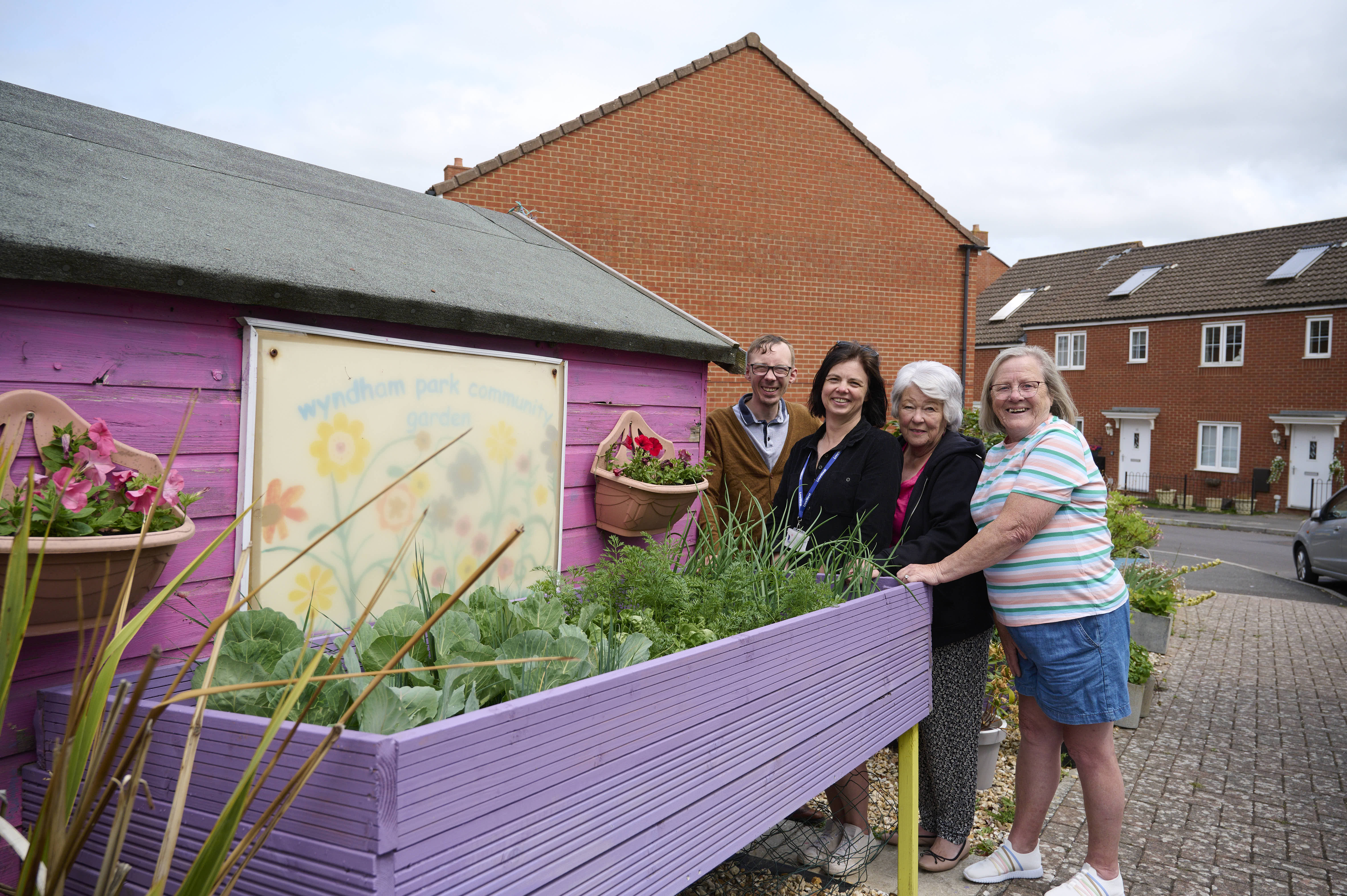 Four residents are stood next to a garden shed smiling, displaying community