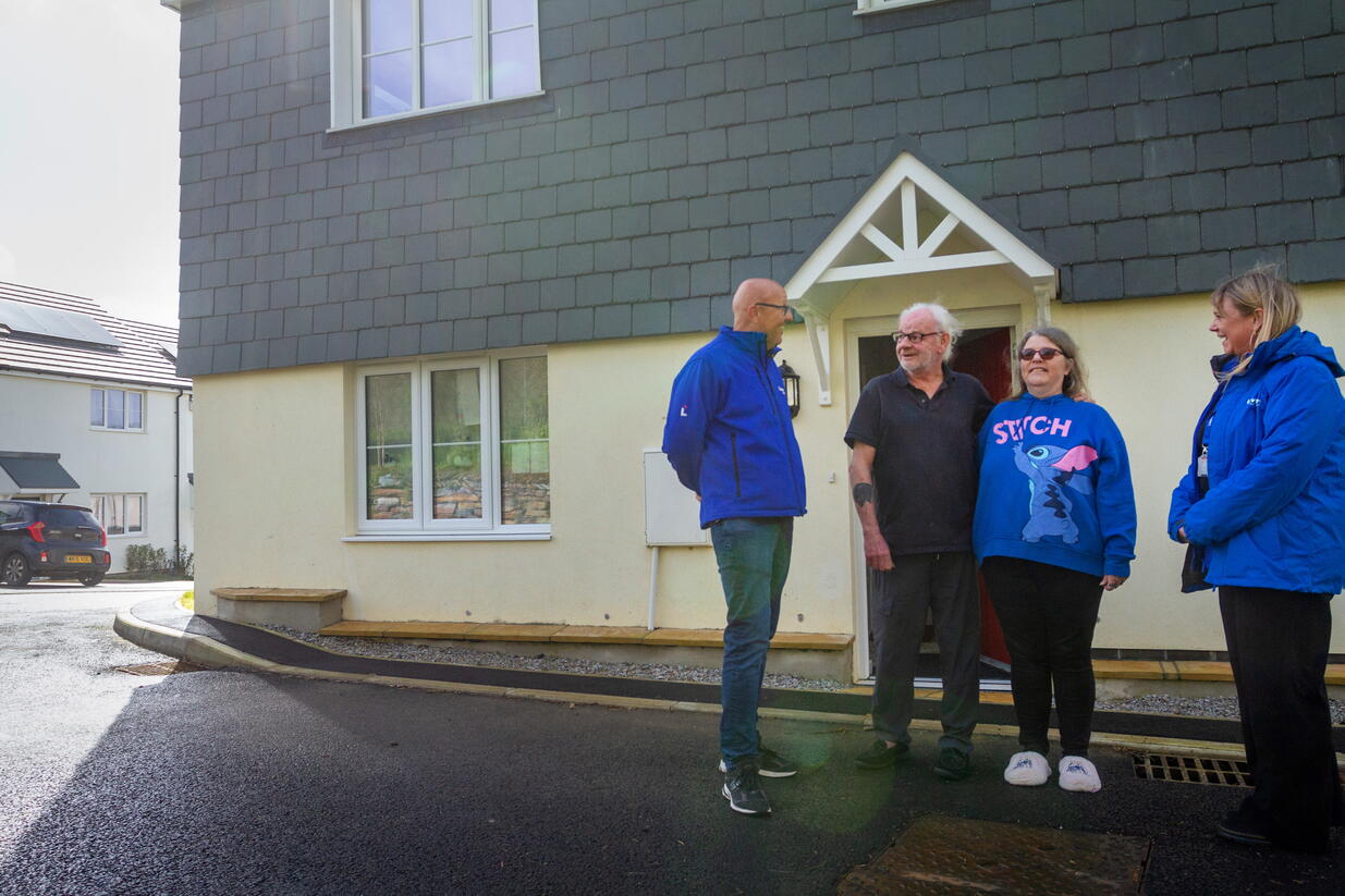 Four people are standing and talking outside a house on a sunny day.