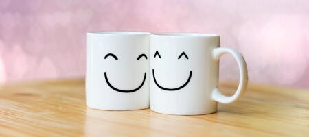 Two mugs on a table with smiley faces on