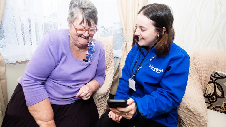 Image of a LiveWest colleague showing a customer how to use the portal on a mobile phone.