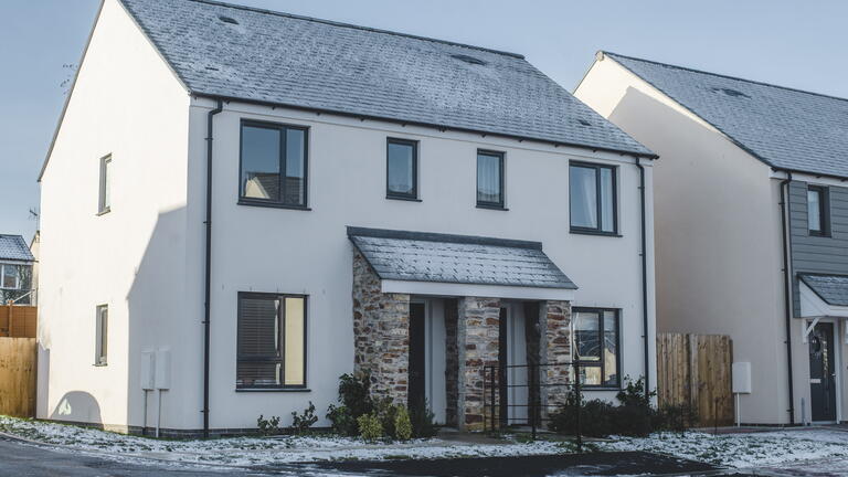 The image shows a two-storey house with a light dusting of snow on the roof and ground, situated in a quiet residential area.