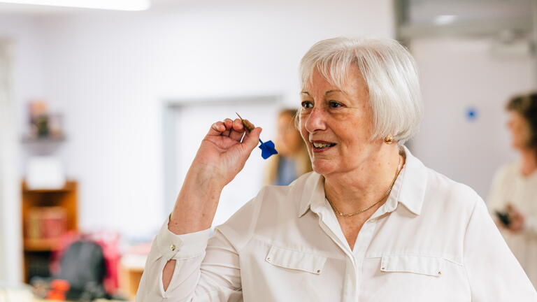 A woman is holding a dart and preparing to throw it in a room that appears to be a casual or recreational space.