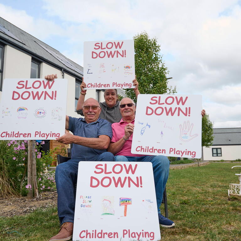 Three men are holding up DIY 'slow down' signs