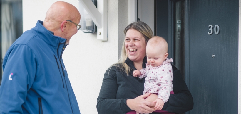 LiveWest colleague talking to a woman holding a baby outside the front door of a house.