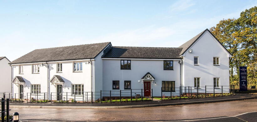Modern semi-detached houses with white walls, black windows, and a red front door on a sunny day.