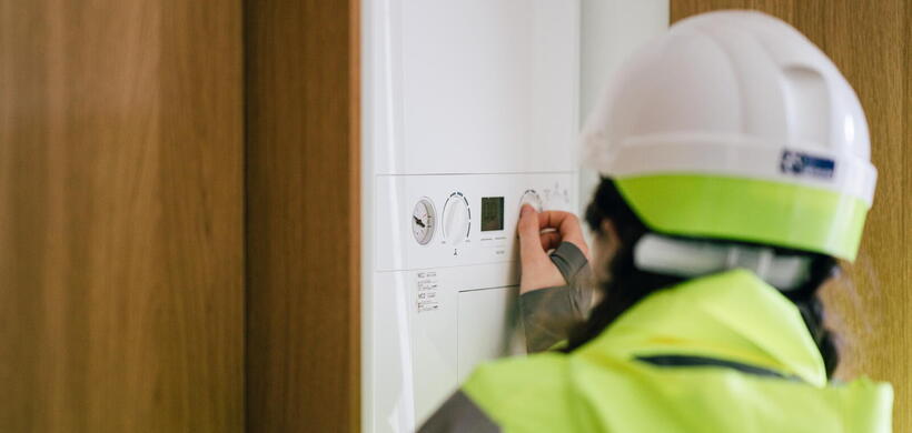 Image of someone wearing a hard hat and a bright yellow jacket adjusting a boiler. 