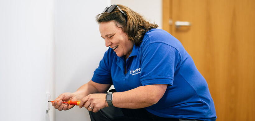 Claire bending down with a screwdriver fixing a repair.