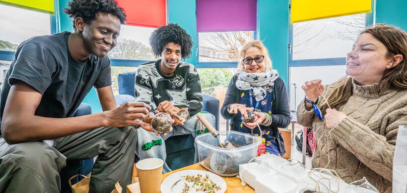 Four people sit together in a bright room, smiling and making decorations on a table.