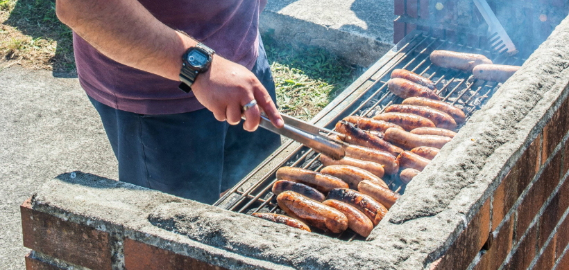A man is cooking sausages on a barbecue at an outdoor event.
