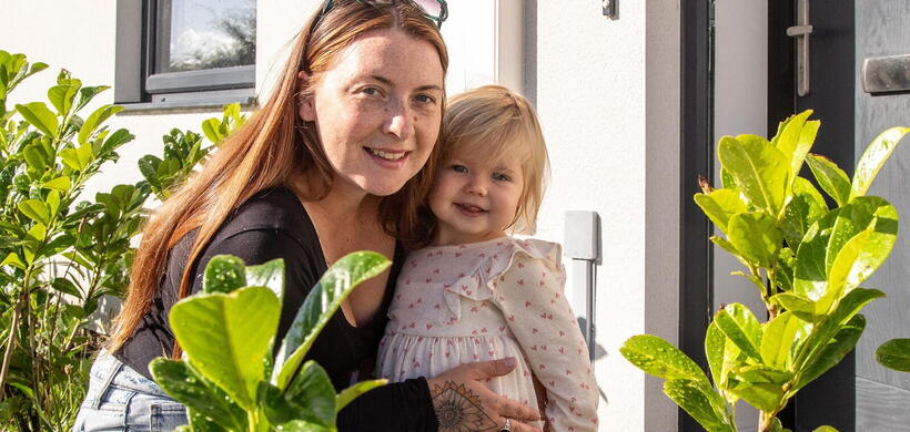 A customer is kneeling down smiling with her daughter in front of her home.