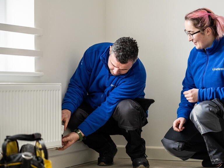 Two LiveWest colleagues carrying out a repair to a radiator in a customer home. 
