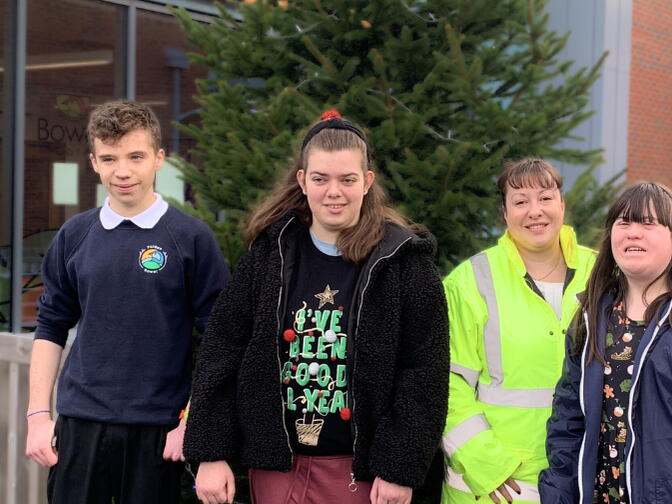 Local school students smiling in front of their new Christmas tree, donated by us.