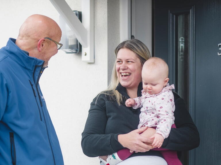 LiveWest colleague talking to a woman holding a baby outside the front door of a house.