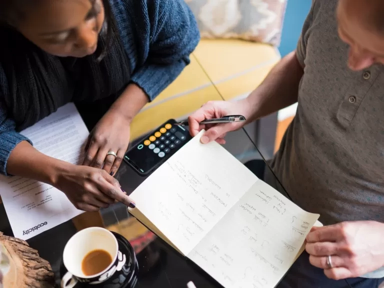 Two people sat at a desk looking at a notepad. 