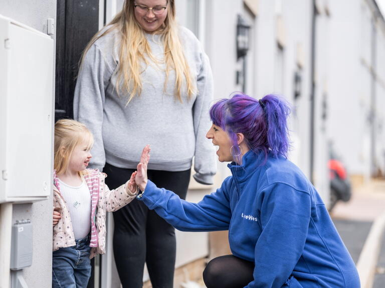 LiveWest colleague high fiving a child outside a house, with the mother standing next to the child. 