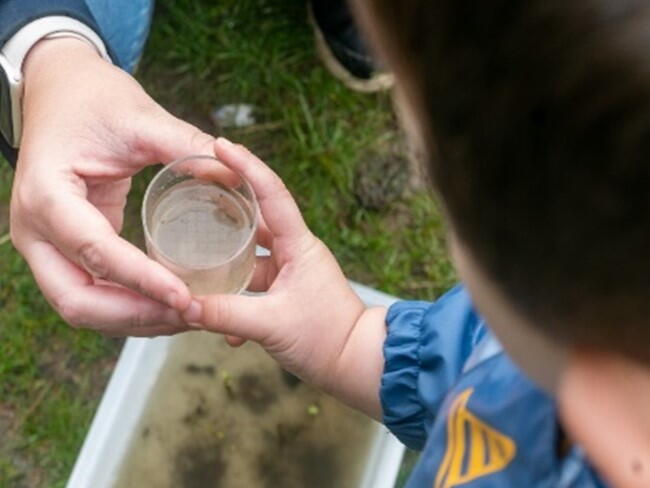 A child giving a small glass container to an adult outside. Image QLPS by Jon Barrett.