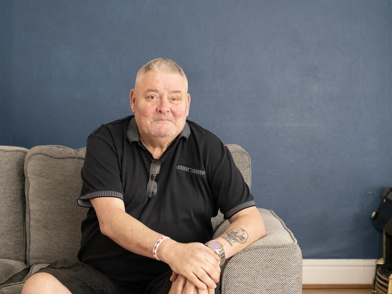 An image of Mark, a military veteran and LiveWest resident, smiling at the camera on the sofa.