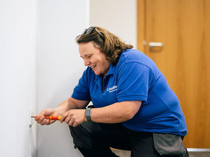 Claire bending down with a screwdriver fixing a repair.