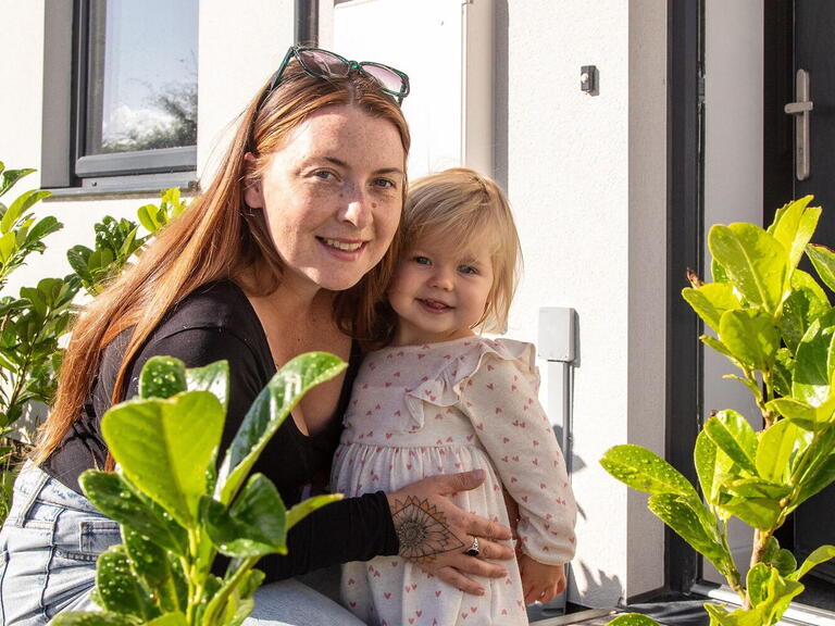 A customer is kneeling down smiling with her daughter in front of her home.