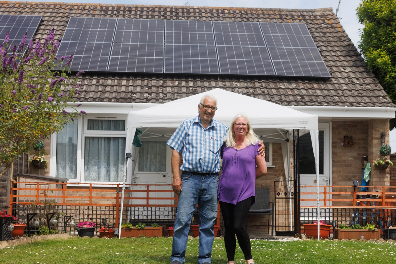 Malcolm and Michelle stood outside their home with solar panels on the roof.