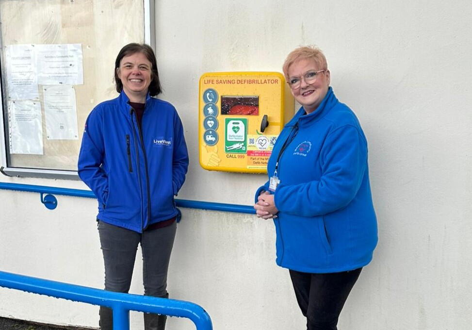 Image of LiveWest colleague and community member smiling in front of the new defibrillato