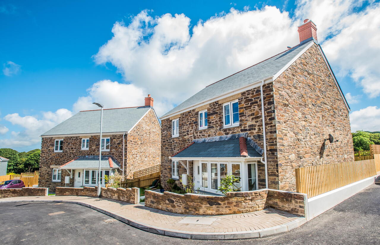 Image shows two houses on a curved road on a bright sunny day.