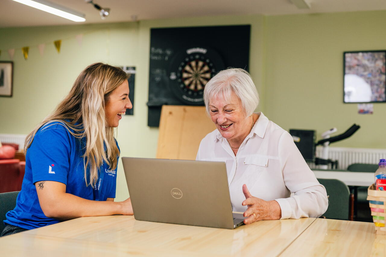 Image shows a LiveWest colleague and customer sat at a table looking at a laptop.