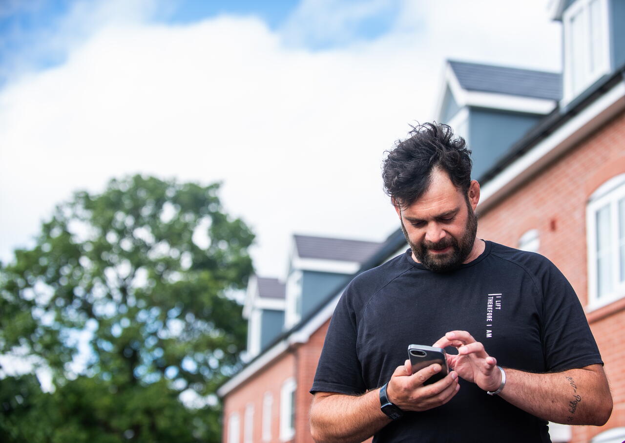 A man is using his phone outside near a row of houses on a clear day.