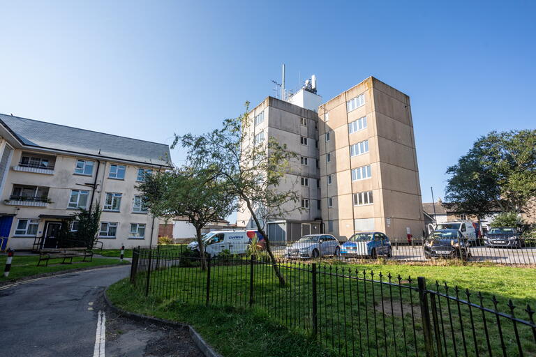 The image shows a quiet street between residential buildings on a sunny day.