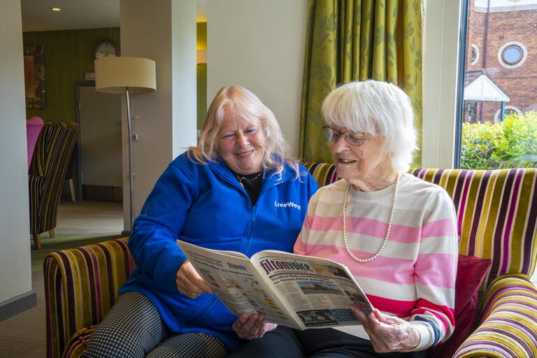 A LiveWest colleague and customer are sat on a sofa smiling.