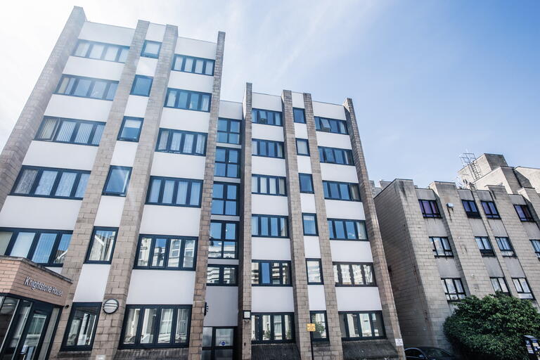 The image shows a tall office building on a clear day, with large windows and a modern, clean design.