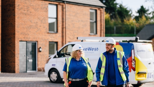 Two LiveWest colleagues wearing safety equipment walking away from their van whilst smiling. 