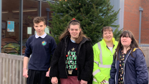 Local school students smiling in front of their new Christmas tree, donated by us.