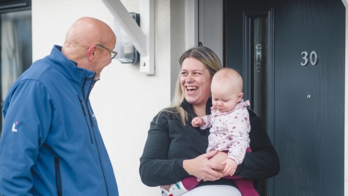 LiveWest colleague talking to a woman holding a baby outside the front door of a house.