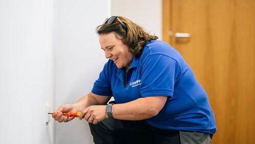 Image shows apprentice, Claire, working on a plug socket and smiling whilst wearing LiveWest uniform