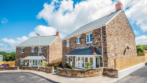 Image shows two houses on a curved road on a bright sunny day.