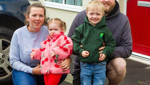 Caitlin, Chris and children smiling outside their front door.