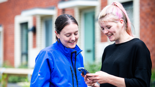 LiveWest colleague and resident are looking at a phone and smiling.
