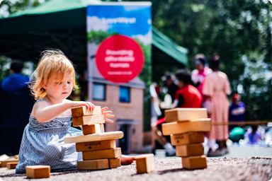 Child playing with building blocks at a LiveWest event, outdoors in the sun.