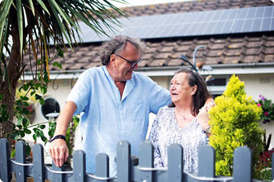 LiveWest customers smiling at each other in front of their LiveWest bungalow with solar panels, on a sunny day.