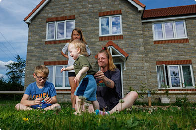 LiveWest customer, young female mum in sat in front of her LiveWest house on the grass playing with her three children.