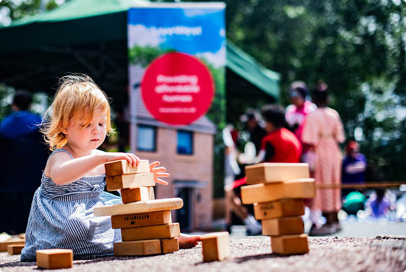 Child playing with building blocks at a LiveWest event, outdoors in the sun.