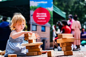 Child playing with building blocks at a LiveWest event, outdoors in the sun.