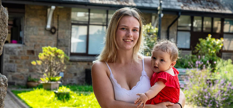 Female customer mother holding her baby in a sunny courtyard.