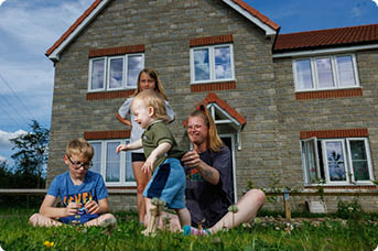 LiveWest customer, young female mum in sat in front of her LiveWest house on the grass playing with her three children.